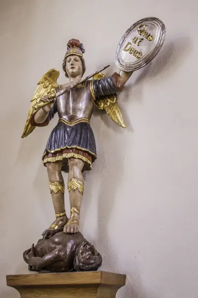 Erzengel Michael in Rüstung mit Schild „Quis ut Deus“ und Speer, den Fuß auf dem Kopf einer dunkelhäutigen, menschengestaltigen Teufelsfigur