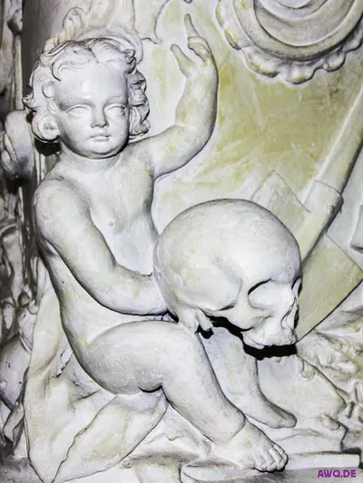 Steinerner Putto, der lächelnd einen menschlichen Totenschädel im Arm hält