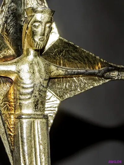 Goldene, stark stilisierte Christusfigur mit ausgebreiteten Armen an einem modernen Kruzifix