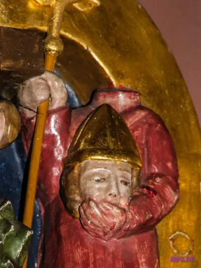 Bemaltes Relief einer blutverschmierten Gestalt mit spitzer goldener Mütze, die Hand vor den Mund geschlagen
