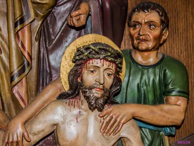 Kreuzwegrelief: blutüberströmter Jesus mit Dornenkrone wird von einem Helfer gestützt
