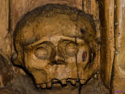 In Holz geschnitzter Totenschädel mit leeren Augenhöhlen an einem verwitterten Balken