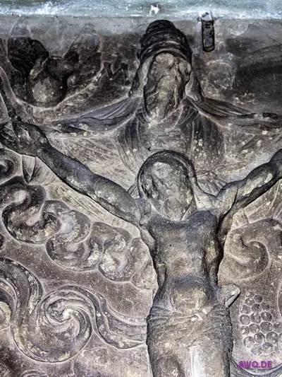 Stark verwittertes Steinrelief einer Kreuzigungsszene mit Christusfigur und Wolkenranken