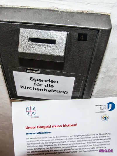 Opferstock mit Aufschrift „Spenden für die Kirchenheizung“, davor eine Unterschriftenliste zum Erhalt des Bargelds