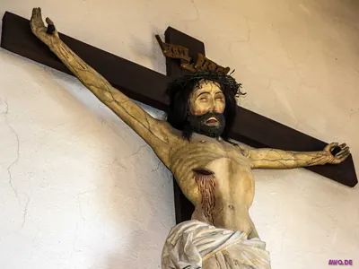 Holzkruzifix mit Dornenkrone und stark blutender Seitenwunde vor weißer Kirchenwand