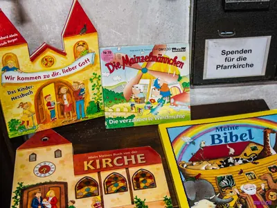 Kinderbücher über Kirche und Bibel im Schriftenstand, dahinter ein Opferstock „Spenden für die Pfarrkirche“