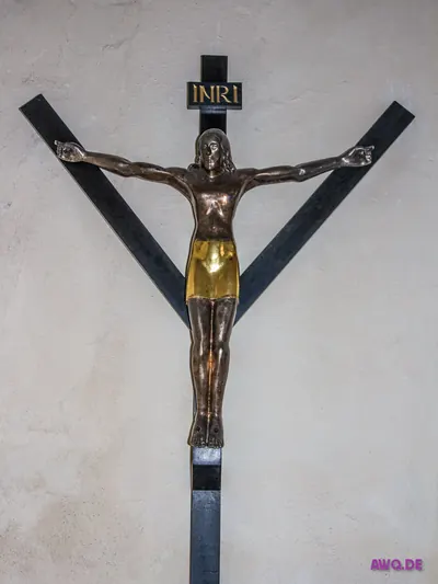 Modernes Metallkruzifix mit INRI-Tafel und goldenem Lendentuch an dunklem Balkenkreuz
