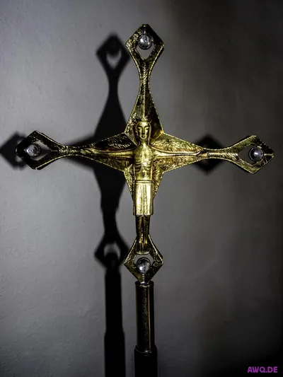 Vergoldetes modernes Vortragekreuz mit stilisierter Christusfigur und starkem Schattenwurf