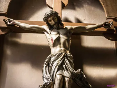 Kruzifixfigur mit Dornenkrone und Seitenwunde vor einer Wandnische, kunstvoll drapiertes Lendentuch