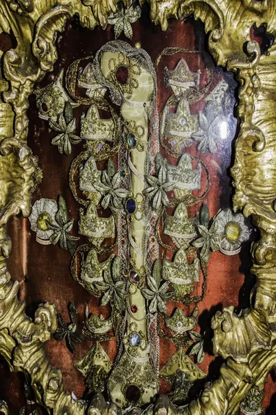 Reliquienrahmen mit Knochen, Goldborten und Schmucksteinen hinter Glas