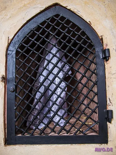 Vergittertes Fenster eines Beinhauses, dahinter gestapelte menschliche Knochen