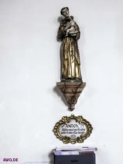 Figur des heiligen Antonius über einer Tafel „St. Antonius, nimm meine Gabe und bitte für mich“ und einem Opferstock