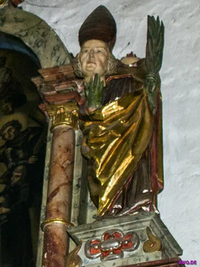 Bemalte Bischofsfigur mit Mitra und Palmzweig hinter einer roten Marmorsäule auf einem Altar
