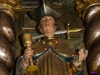 Figur eines Geistlichen mit Birett und Kelch, ein Schwert steckt quer in seinem Hals