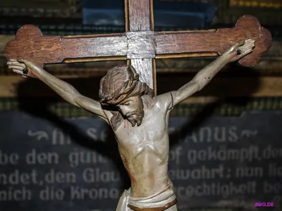 Altes Holzkruzifix vor einer Gedenktafel mit goldener Inschrift