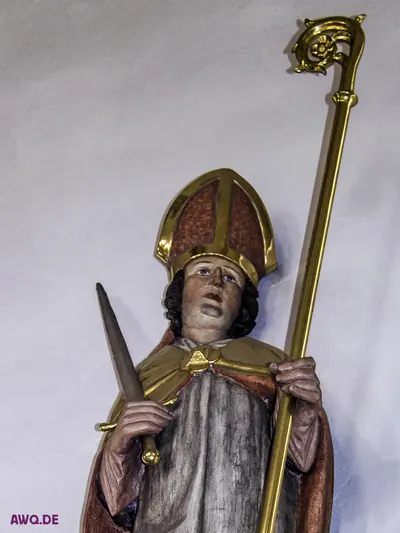 Bemalte Bischofsfigur mit Mitra und goldenem Krummstab, in der Hand ein großes Messer