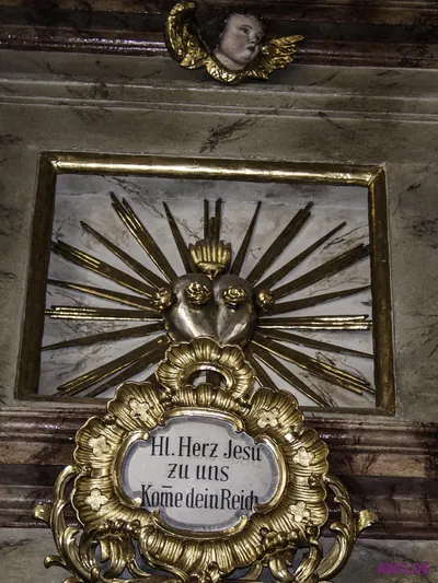 Silbernes Herz-Jesu-Relief im Strahlenkranz über einer Kartusche mit der Inschrift „Hl. Herz Jesu zu uns“