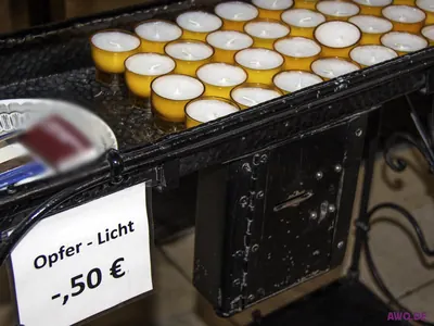 Ständer mit Opferkerzen und einem Schild „Opfer-Licht -,50 €“ neben dem Geldeinwurf