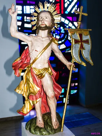 Figur des auferstandenen Christus mit Siegesfahne und Strahlenkranz vor einem Buntglasfenster