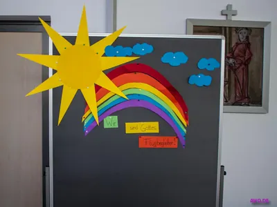 Pinnwand mit Sonne und Regenbogen aus Papier, Aufschrift „Wir sind Gottes Flugbegleiter!“