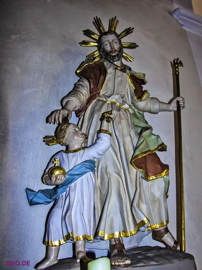 Heiligenfigur mit Strahlenkranz, die einem Kind mit Weltkugel die Hand auf den Kopf legt