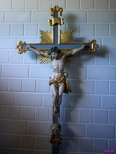 Barockes Vortragekreuz mit Christusfigur und goldenen Strahlen vor einer weißen Ziegelwand