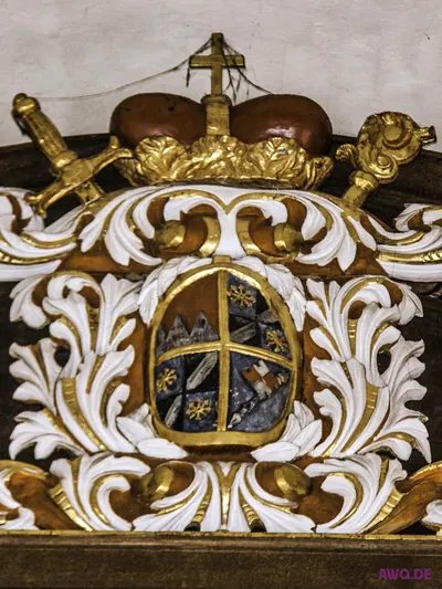 Geschnitztes Wappen mit Krone, Schwert und Bischofsstab über weißem Rankenwerk