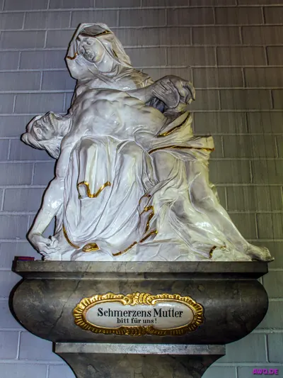 Weiße Pietà auf einem Sockel mit der Aufschrift „Schmerzensmutter, bitt für uns!“