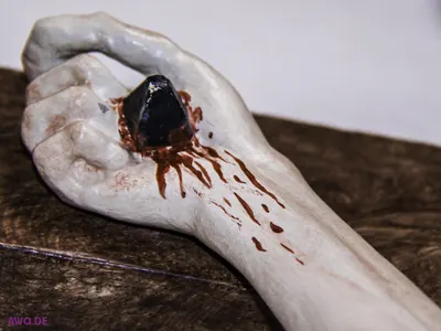 Nahaufnahme einer durchnagelten Hand mit Blutspuren auf hellem Holz