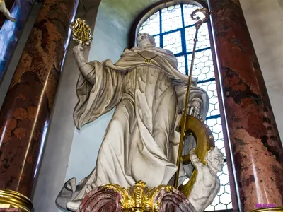 Weiße Heiligenfigur mit goldenem Krummstab und flammendem Herz, darunter eine gehörnte Teufelsgestalt am Rad