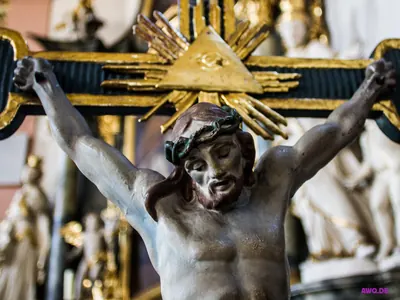 Kruzifixfigur vor einem goldenen Dreieck mit dem Auge Gottes und Strahlenkranz