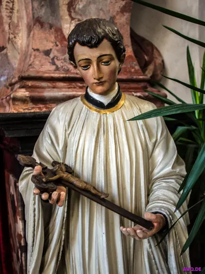 Figur eines jungen Klerikers im Chorhemd, der ein Kruzifix in den Händen hält