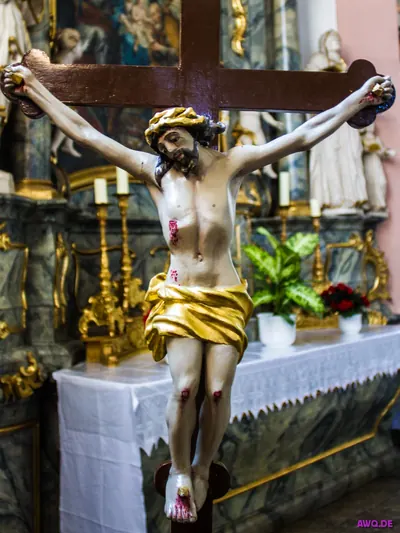 Kruzifix mit goldenem Lendentuch und blutenden Wunden vor einem Seitenaltar