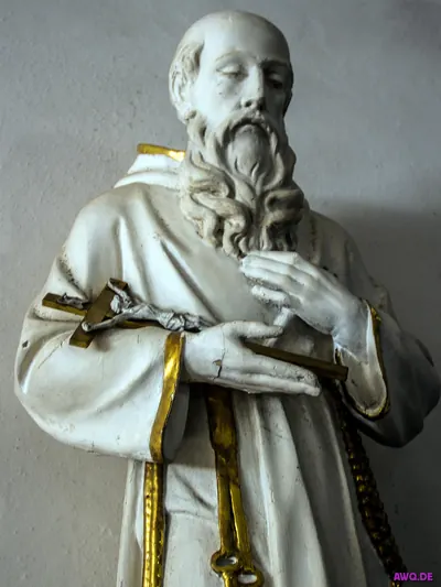 Weiße Ordensfigur mit langem Bart, die ein kleines Kruzifix in den Händen hält