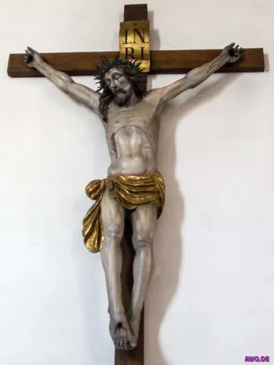 Kruzifix mit INRI-Tafel, Dornenkrone und goldenem Lendentuch an weißer Wand