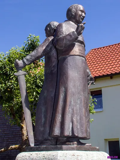 Bronzedenkmal eines Geistlichen mit erhobenem Zeigefinger vor einem Wohnhaus