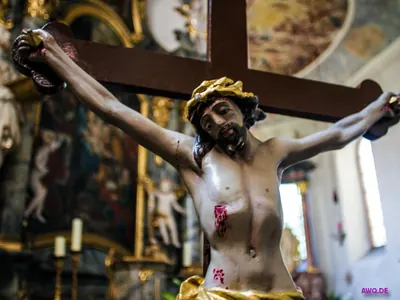 Kruzifixfigur mit goldener Dornenkrone und roten Wundmalen vor einem barocken Kirchenraum