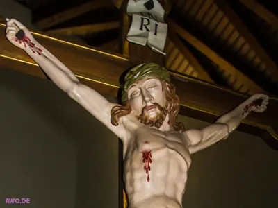 Kruzifixfigur mit langen Haaren und Dornenkrone, Blut tropft aus Händen und Seitenwunde