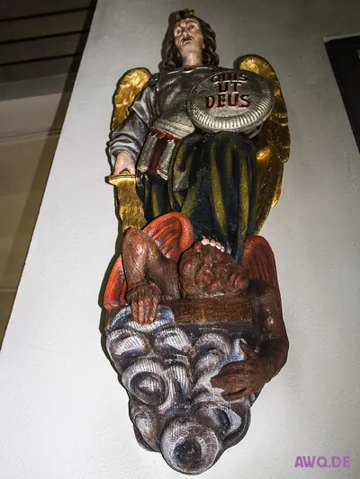 Wandrelief des Erzengels Michael mit Schild „Quis ut Deus“ über einem gestürzten roten Teufel