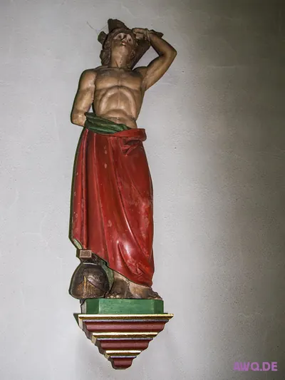 Wandfigur eines halbnackten Märtyrers mit rotem Tuch, die Arme über den Kopf gelegt, zu seinen Füßen ein Helm