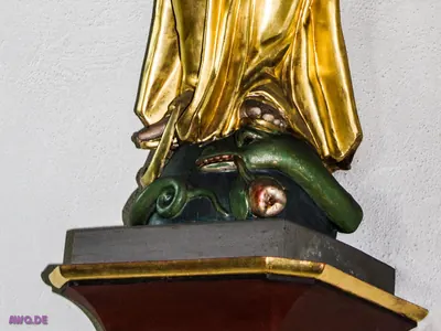 Detail: der Fuß einer vergoldeten Figur steht auf einem grünen Drachen, der einen roten Apfel im Maul hält