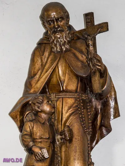 Holzfigur eines bärtigen Ordensmannes, der ein Kruzifix hält, neben ihm ein Kind