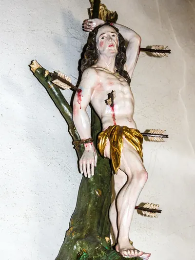Sebastiansfigur am Baumstamm mit Pfeilen in Brust, Bein und Arm, Blut an den Wunden
